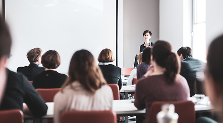 Image showing Female speaker giving presentation in lecture hall at university workshop . Participants listening to lecture and making notes. Scientific conference event