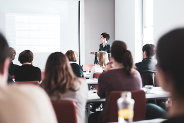 Image showing Female speaker giving presentation in lecture hall at university workshop . Participants listening to lecture and making notes. Scientific conference event