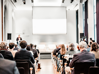 Image showing Speaker giving a talk in conference hall at business event. Rear view of unrecognizable people in audience at the conference hall. Business and entrepreneurship concept.