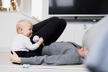 Image showing Happy family moments. Mother lying comfortably on children's mat playing with her baby boy watching and suppervising his first steps. Positive human emotions, feelings, joy.