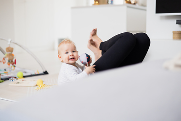 Image showing Happy family moments. Mother lying comfortably on children's mat playing with her baby boy watching and suppervising his first steps. Positive human emotions, feelings, joy.