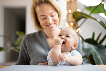 Image showing Portrait of young mother cuddling her adorable little child while sitting at the table at home. Sensory stimulation for baby development