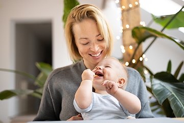 Image showing Portrait of young mother cuddling her adorable little child while sitting at the table at home. Sensory stimulation for baby development