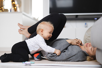 Image showing Happy family moments. Mother lying comfortably on children's mat playing with her baby boy watching and suppervising his first steps. Positive human emotions, feelings, joy.