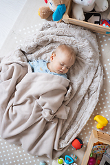 Image showing Cute infant baby boy sleeping on playing mat covered with warm cosy blanket.