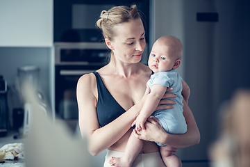 Image showing Pretty young mother holding her newborn baby boy standing near kitchen window at home