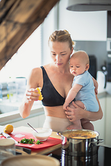 Image showing Woman cooking while holding four months old baby boy in her hands