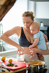 Image showing Woman cooking while holding four months old baby boy in her hands