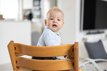 Image showing Happy infant sitting in traditional scandinavian designer wooden high chair and laughing out loud in modern bright home. Cute baby smile.