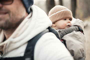 Image showing Sporty father carrying his infant son wearing winter jumpsuit and cap in backpack carrier hiking in autumn forest.
