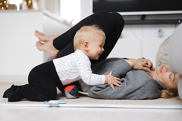 Image showing Happy family moments. Mother lying comfortably on children's mat playing with her baby boy watching and suppervising his first steps. Positive human emotions, feelings, joy.