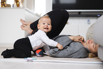 Image showing Happy family moments. Mother lying comfortably on children's mat playing with her baby boy watching and suppervising his first steps. Positive human emotions, feelings, joy.