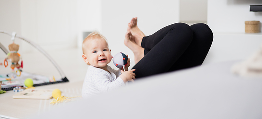 Image showing Happy family moments. Mother lying comfortably on children's mat playing with her baby boy watching and suppervising his first steps. Positive human emotions, feelings, joy.