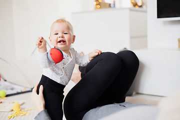 Image showing Happy family moments. Mother lying comfortably on children's mat watching and suppervising her baby boy playinghis in living room. Positive human emotions, feelings, joy