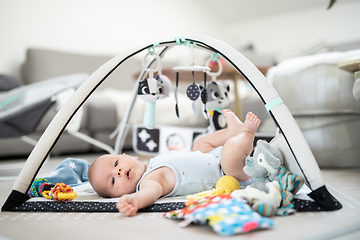 Image showing Cute baby boy playing with hanging toys arch on mat at home Baby activity and play center for early infant development. Baby playing at home