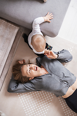 Image showing Happy family moments. Mother lying comfortably on children's mat playing with her baby boy watching and suppervising his first steps. Positive human emotions, feelings, joy.