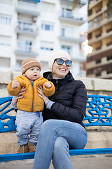 Image showing Young mother with her cute infant baby boy child on bench in city park.