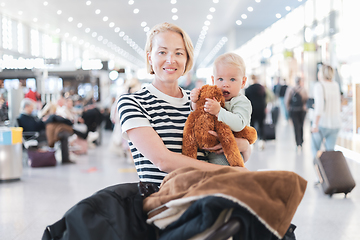 Image showing Mother traveling with child, holding his infant baby boy at airport terminal waiting to board a plane. Travel with kids concept.