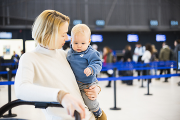 Image showing Motherat travelling with his infant baby boy child, walking, pushing baby stroller and luggage cart at airport terminal station. Travel with child concept.