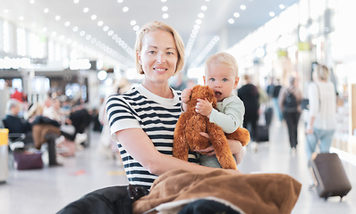 Image showing Mother traveling with child, holding his infant baby boy at airport terminal waiting to board a plane. Travel with kids concept.