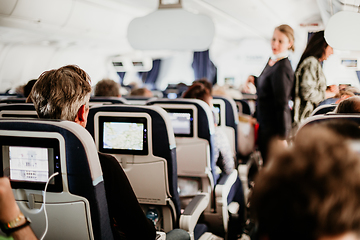 Image showing Interior of airplane with passengers on seats and stewardess in uniform walking the aisle, serving people. Commercial economy flight service concept.