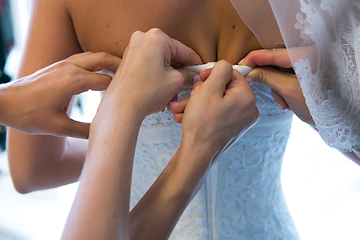 Image showing Hands of girlfriends helping the bride to dress her dress