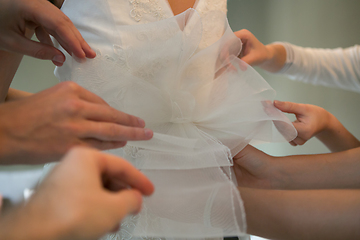 Image showing Hands of girlfriends helping the bride to dress her dress