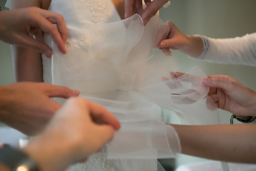 Image showing Hands of girlfriends helping the bride to dress her dress