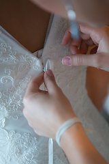 Image showing Hands of girlfriends helping the bride to dress her dress