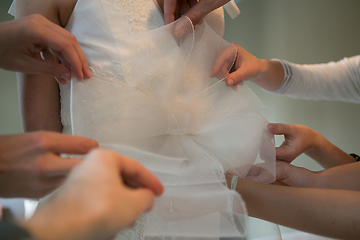 Image showing Hands of girlfriends helping the bride to dress her dress