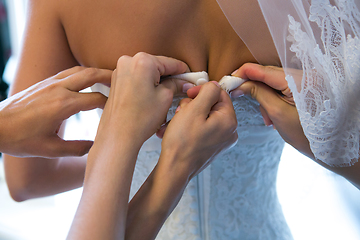 Image showing Hands of girlfriends helping the bride to dress her dress