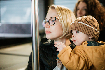 Image showing Mother carries her child while standing and holding on to the bus. Mom holding her infant baby boy in her arms while riding in a public transportation. Cute toddler boy traveling with his mother.