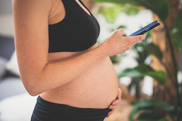 Image showing Pregnancy and technoloy supported healthy lifestyle concept. Cheerful happy pregnant woman using smart phone application at home.