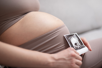 Image showing Pregnant woman belly. Pregnancy Concept. Pregnant tummy close up. Detail of pregnant woman relaxing on comfortable sofa at home.