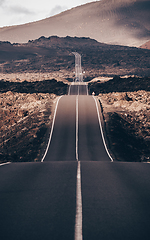 Image showing Endless road on a volcano in Timanfaya National Park in Lanzarote in the Canary Islands with a continuous line, black volcanic rocks on the side and volcanoes in mist in background.