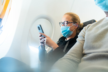 Image showing A young woman wearing face mask, using smart phone while traveling on airplane. New normal travel after covid-19 pandemic concept.