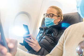 Image showing A young couple wearing face mask, using smart phone while traveling on airplane. New normal travel after covid-19 pandemic concept.