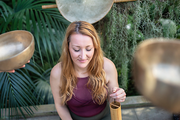 Image showing Yoga concept, meditation and sound therapy. Beautiful young caucasian woman surrounded by copper tibetan singing bowls and instruments.