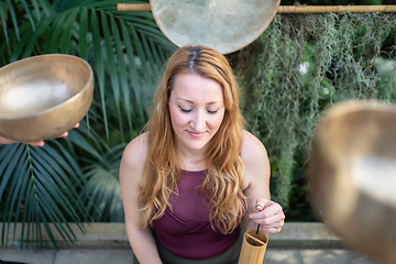 Image showing Yoga concept, meditation and sound therapy. Beautiful young caucasian woman surrounded by copper tibetan singing bowls and instruments.