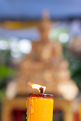 Image showing Candlelight burning in front of Buddha statue. Focus on candle frame, buddha blured in background.