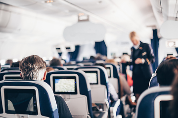 Image showing Interior of airplane with passengers on seats and stewardess in uniform walking the aisle, serving people. Commercial economy flight service concept.