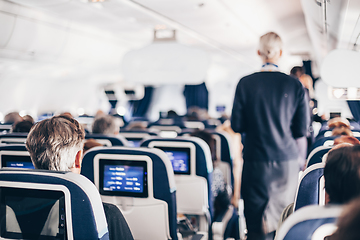 Image showing Interior of airplane with passengers on seats and stewardess in uniform walking the aisle, serving people. Commercial economy flight service concept.