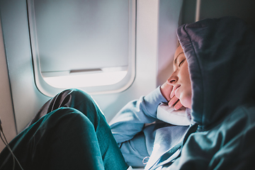 Image showing Tired blonde casual caucasian woman wearing sporty hoodie napping on seat while traveling by airplane. Commercial transportation by planes. Authentic image of real people.