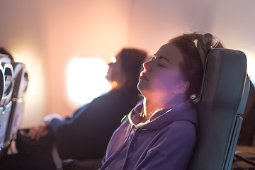 Image showing Out of fokus image of tired blonde casual caucasian woman wearing sporty hoodie napping on seat while traveling by airplane. Commercial transportation by planes. Authentic image of real people.