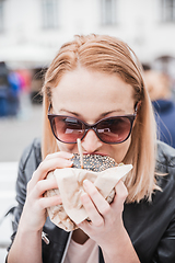 Image showing Pretty young blonde funny woman eating hamburger outdoor on the street