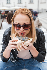 Image showing Pretty young blonde funny woman eating hamburger outdoor on the street.