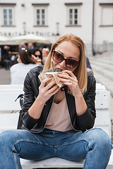 Image showing Pretty young blonde funny woman eating hamburger outdoor on the street