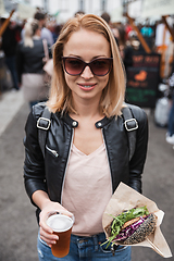 Image showing Beautiful young woman holding delicious organic salmon vegetarian burger and homebrewed IPA beer on open air beer an burger urban street food festival in Ljubljana, Slovenia.