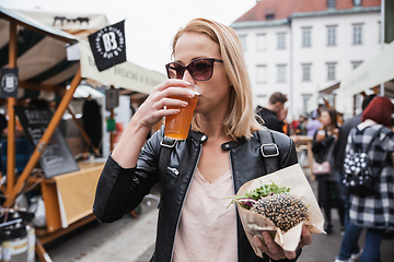 Image showing Beautiful young woman holding delicious organic salmon vegetarian burger and drinking homebrewed IPA beer on open air beer an burger urban street food festival in Ljubljana, Slovenia.