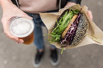 Image showing Close up of woman hands holding delicious organic salmon vegetarian burger and homebrewed IPA beer on open air beer an burger urban street food festival in Ljubljana, Slovenia.